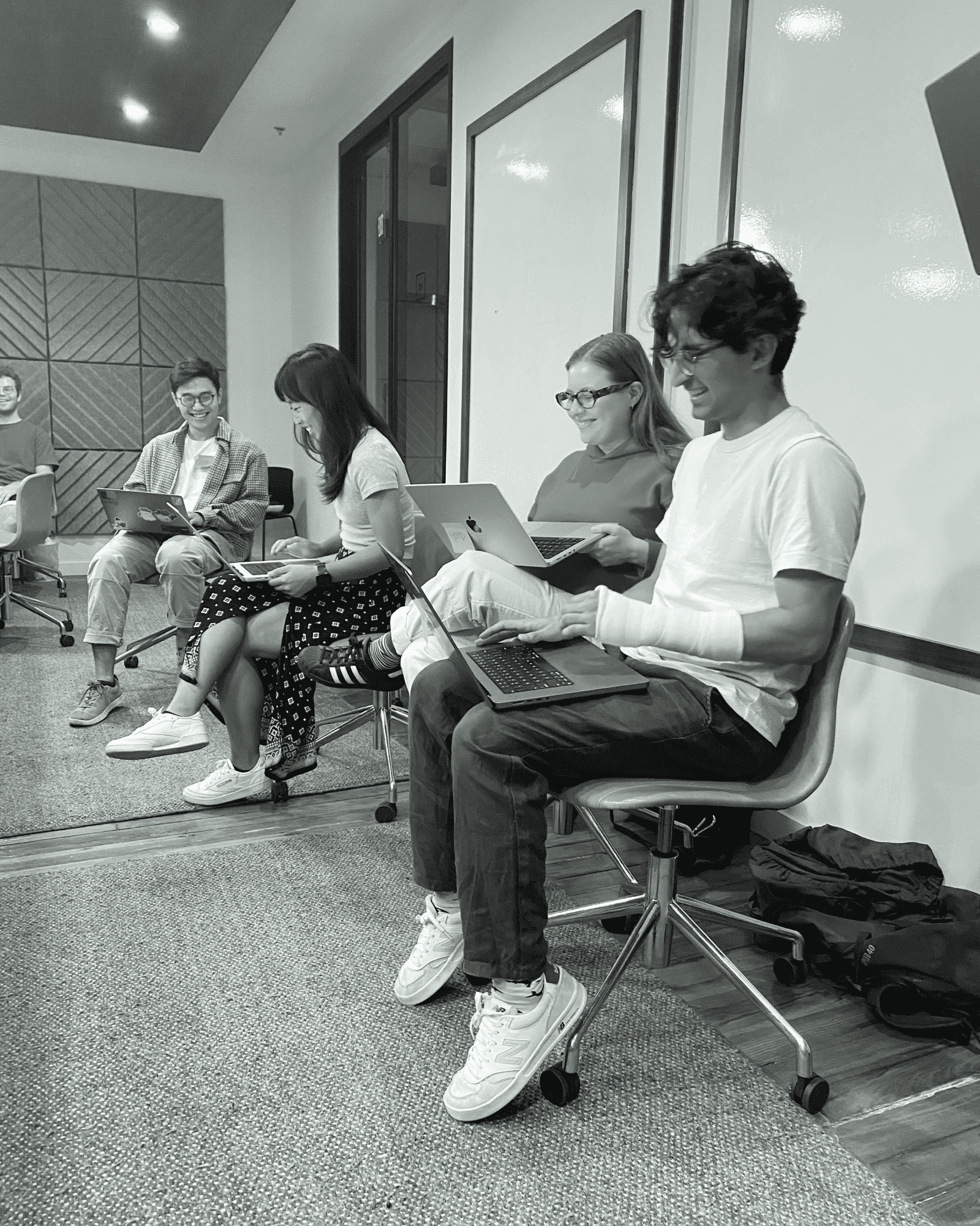 A group of people sitting on chairs in a conference room, working on laptops and engaging in discussion.