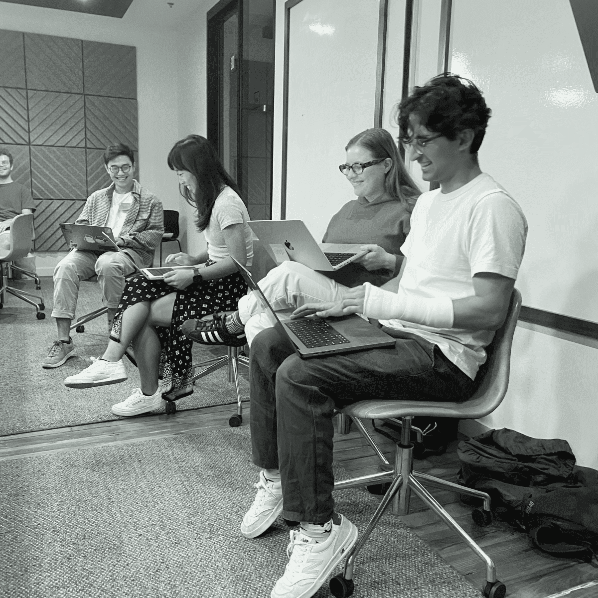 A group of people sitting on chairs in a conference room, working on laptops and engaging in discussion.